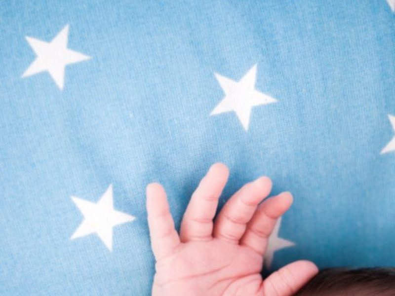 Mão de um recém-nascido sobre manta azul com estrelas